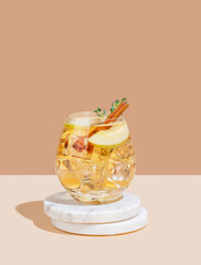 Apple cocktail or cider in a glass with ice, cinnamon and thyme, on a marble stand
