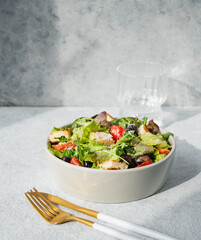 Salad with lettuce, tomatoes, croutons, olives and parmesan cheese in a bowl on a light background