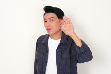 Young Asian man listening to something with hand on ear gesture
