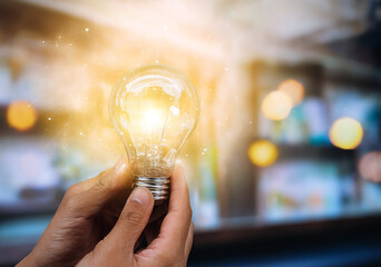 A creative shot of a human hand gently holding a glowing lightbulb