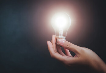 A creative shot of a human hand gently holding a glowing lightbulb