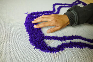 Part of craftswoman checking thread on canvas while weaving rug 
