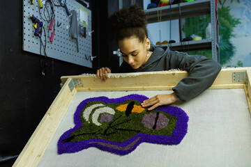 Young african american craftswoman looking at handmade rug in studio
