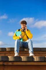 Young student talking on smartphone and holding folder outdoors