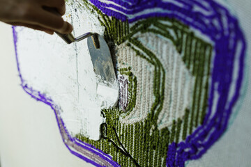 Close up of craftswoman with trowel applying glue on handmade rug 
