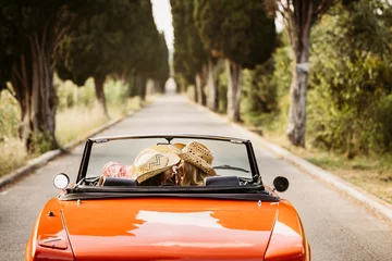 Fotobehang Toscane Two women kissing while driving orange convertible car on a country road  © Jordi Salas
