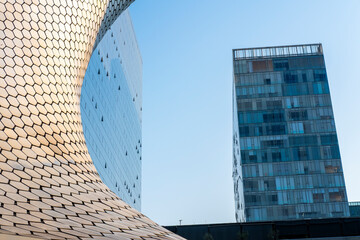 Modern glass building with curved steel facade reflecting sunlight and surrounding architecture in a contemporary urban environment