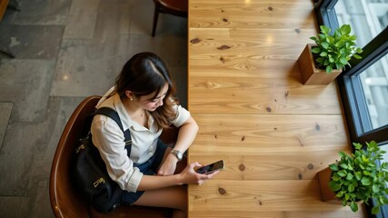 Young Woman Using Smartphone While Sitting at a Wooden Table