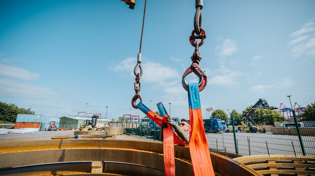 Construction worker supervising crane lifting metal rings at industrial site