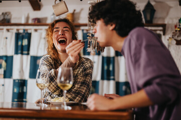 A cheerful moment between two friends sharing laughter and enjoying beverages in an intimate and warm indoor environment, indicating a relaxed and joyful social interaction.