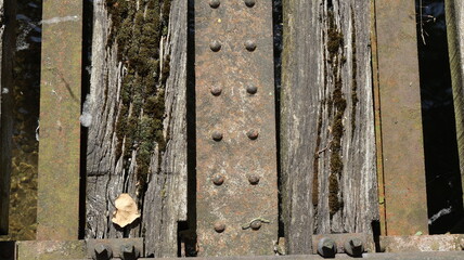 Old construction of wooden plank with moss and rusty metal profiles and fixing screws