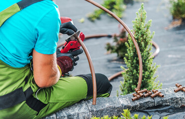Gardener Uses Tool to Cut Irrigation Tubing While Installing System in Green Landscape
