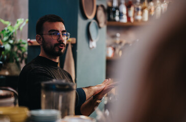 Casual setting featuring a man at a lounge bar, engaging in conversation with others, surrounded by modern interior decor and drinks, highlighting a relaxed and vibrant social atmosphere.