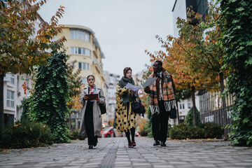 Obraz premium Three young business people walking along an urban pathway in autumn, holding documents and discussing ideas, surrounded by modern architecture.