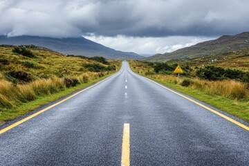 Empty asphalt road stretches into a hazy, mountainous landscape under a cloudy sky