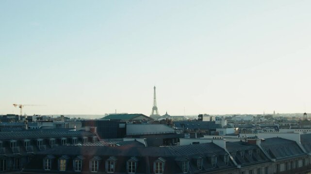 Eiffel tower emerging from parisian rooftops under clear sky