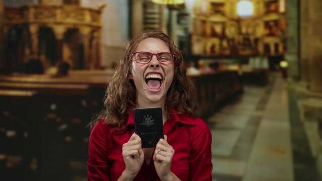 Woman holding australian passport inside church wears red shirt expressing happiness and excitement with indoor religious background highlighting travel and joy.
