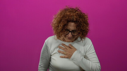 Woman standing with hand on chest against vibrant pink background showing emotion with curly hair...
