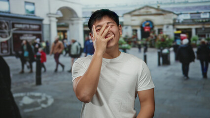 Young man laughing on a busy city street with people walking in the background on a bright day