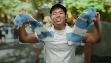 Young man celebrating enthusiastically on a city street wearing a blue and white scarf, expressing...