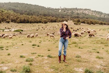 Naklejka premium A woman in a cowboy hat is standing in a field with a herd of sheep