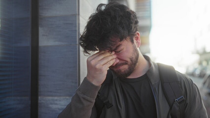 Young man with beard frustrated outdoors on sunny day covering face with hand exuding stress in...