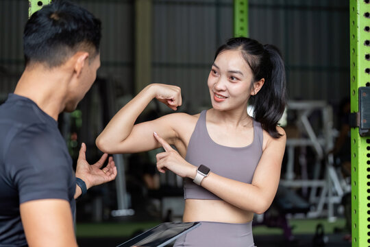 Personal Training Session. Young woman showcasing strength with fitness coach in gym.
