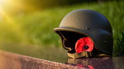 Military helmet with red remembrance poppy placed on marble surface at sunset, tribute to fallen soldiers, war memorial, honoring veterans, national commemoration, symbolic gesture
