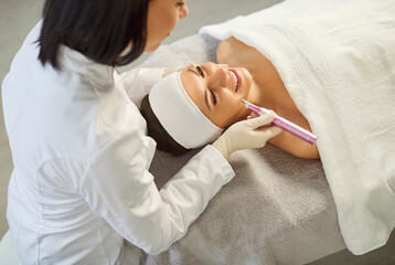 Cosmetologist, dermatologist beautician using dermapen miconeedling roller pen performing female...