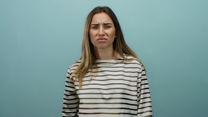 Young woman with blonde hair and striped shirt expressing annoyance against a solid blue background...
