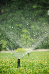 Closeup of automatic lawn sprinklers in action, spraying water over green grass during a sunny day...