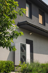 Plakat Dual-fan heat pump unit mounted beside a residential house wall with greenery and modern facade elements in a landscaped garden