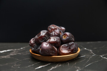 Dates fruit in wooden dish isolated on dark background.