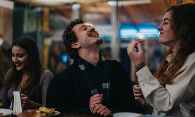 Three friends share food and laugh together at a cozy, warm restaurant setting.