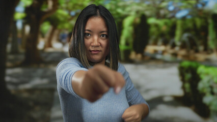 Naklejka premium Young woman practicing martial arts in a park, showcasing strength and focus amidst the tranquil outdoor setting, capturing her dynamic movement and intensity in a natural environment.