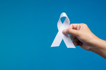 Hand holding white awareness ribbon on blue background, symbol of peace, support, and advocacy.