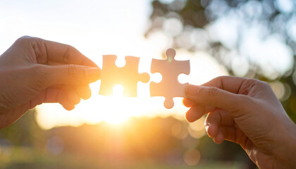 Two hands holding puzzle pieces together against bright sunset, symbolizing teamwork, connection, and partnership in hopeful and warm outdoor setting