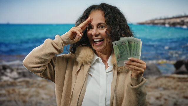 Woman smiling with singapore banknotes at seaside, symbolizing wealth and travel with gesture against scenic ocean background.