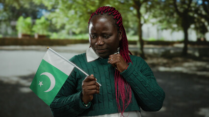 Woman holding pakistan flag outdoors in park with trees in background featuring thoughtful...