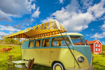 Vintage motor home with sun screen in a typical Swedish landscape with cows and red farm building