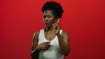 Woman points to herself and gestures no with a finger, standing on an isolated red background,...