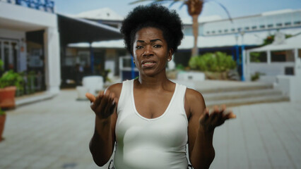 Woman expressing emotions on a street, wearing a white shirt, exhibiting a pensive mood with arms...