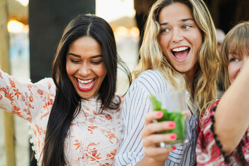 Multiracial happy women friends dancing and drinking mojitos at beach party with dj playing music in background - Summer events and vacation concept - Focus on blond girl face