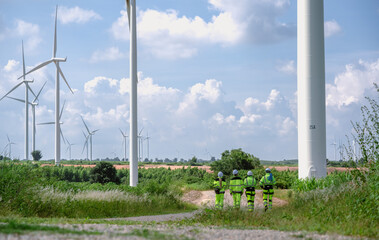 Maintenance engineer team standing at windmills at wind turbine farm. Group of people wear safety...