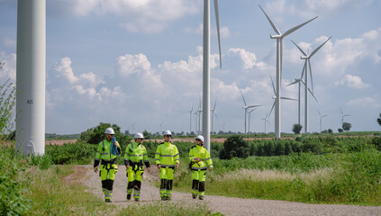 Maintenance engineer team standing at windmills at wind turbine farm. Group of people wear safety...