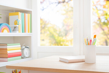 Office supplies in holder and notebook on wooden school desk with copy space in front of blurred classroom window interior background. Original work - no AI used