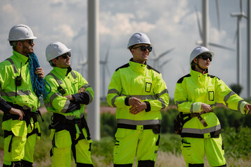 Maintenance engineer team standing at windmills at wind turbine farm. Group of people wear safety...