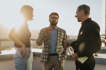 Three business colleagues engage in a lively discussion on a high tower balcony. The sunlight enhances their brainstorming session, highlighting teamwork and innovative thinking in a professional