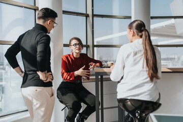 A group of business employees engage in a casual discussion in a modern office kitchen. The bright...
