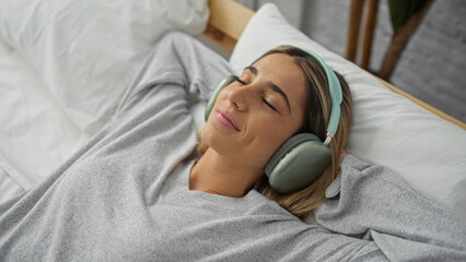 Woman relaxing on bed wearing headphones in a cozy bedroom setting, exuding comfort and tranquility with closed eyes, enjoying a peaceful moment at home.